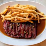 A classic plate of Toronto steak frites topped with herb butter and served with a mountain of crispy golden fries.