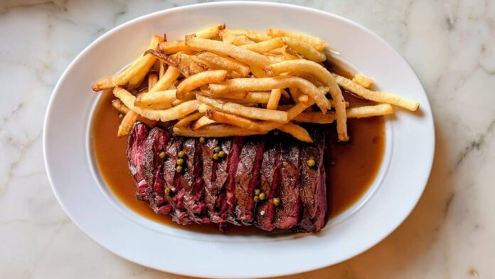 A classic plate of Toronto steak frites topped with herb butter and served with a mountain of crispy golden fries.