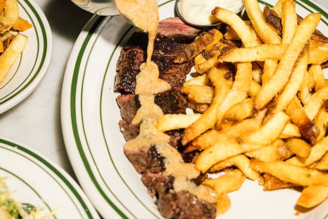 Hanger steak frites topped with herb butter and served with golden fries and garlic aioli at Milou Dundas West.